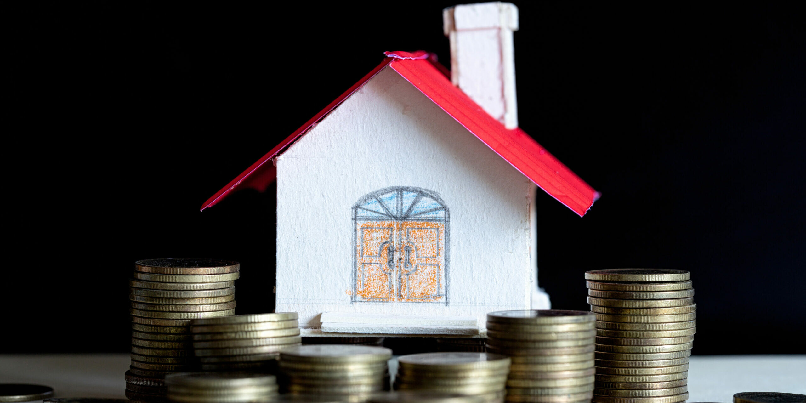 Model of house with coins on wooden table, saving money for buy