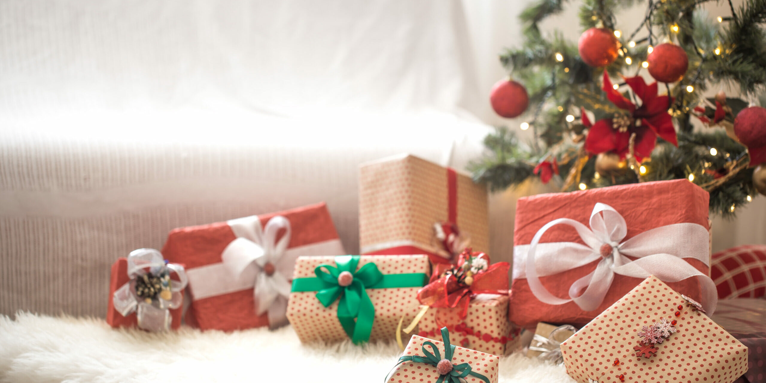 Pile of Christmas presents over light background on wooden table with cozy rug. Christmas decorations